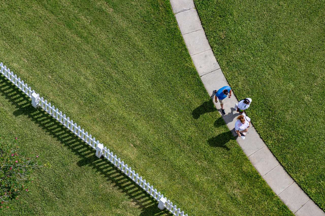 Aerial perspective of individuals strolling along a curved sidewalk beside a white fence in Ponce Inlet, Florida.